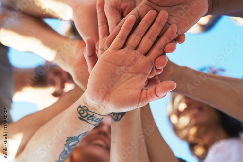 Palms of friends making pile of hands under blue sky outdoors