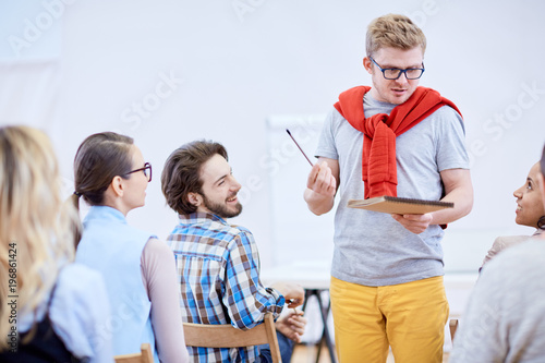 Young speaker with pencil and notepad explaining his ideas to one of students during lecture or seminar