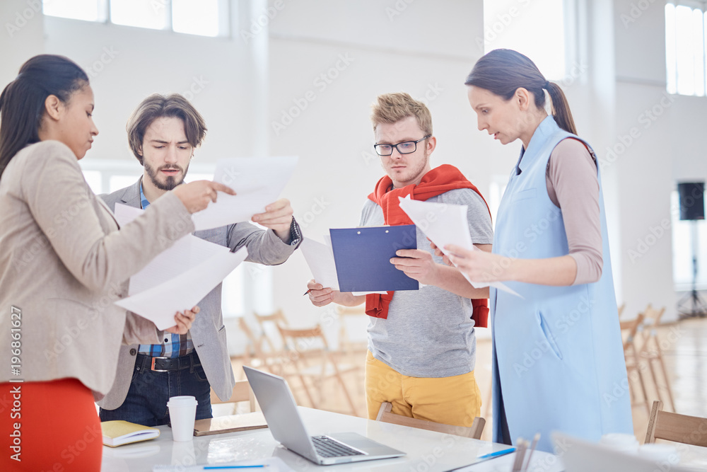 Group of managers with papers standing around table and discussing information Group of managers with papers standing around table and discussing information