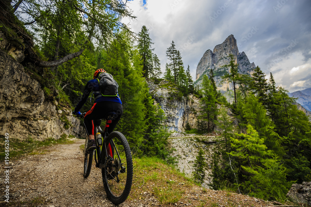 Tourist cycling in Cortina d'Ampezzo, stunning rocky mountains on the background. Woman riding MTB enduro flow trail. South Tyrol province of Italy, Dolomites.