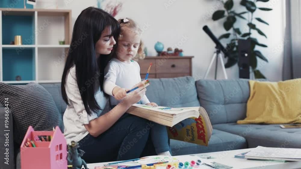 Beautiful mum sits with baby hug painting on paper book together on the sofa at home smiling kid family hobby girl love house coloring mom play art childhood portrait home table artist closeup mother Beautiful mum sits with baby hug painting on paper book together on the sofa at home smiling kid family hobby girl love house coloring mom play art childhood portrait home table artist closeup mother