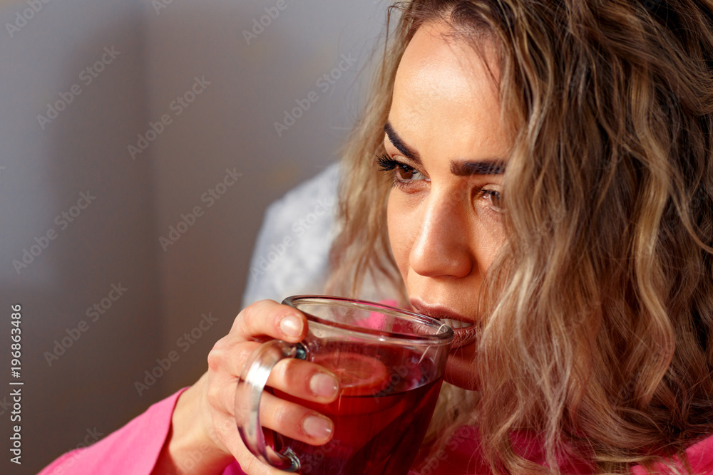 Young ill woman drinking tea with lemon in bed at home, close up. Young ill woman drinking tea with lemon in bed at home, close up.