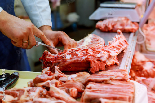 Tableau sur toile Cropped image of male butcher cutting raw meat with knife at counter shop