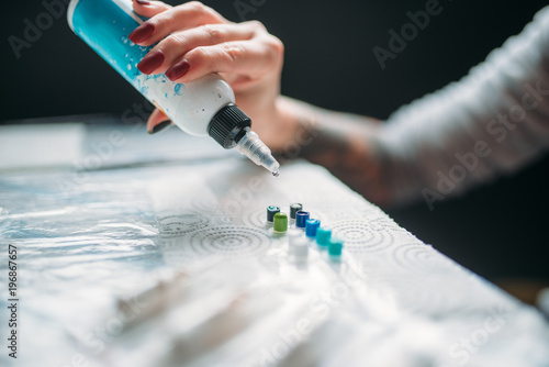 Female tattooist hand with bottle of color ink
