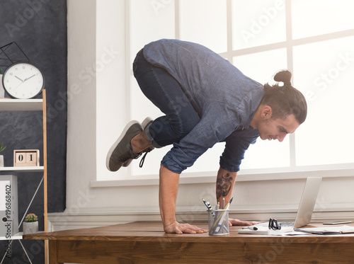 Fototapeta Naklejka Na Ścianę i Meble -  Flexible man practicing yoga at workplace