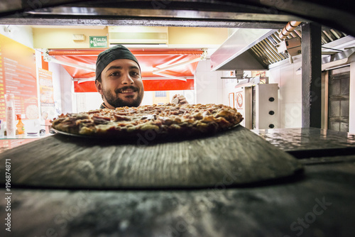 inside view of man cooking a pizza in owen at store photo