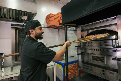 Arab turkish man preparing pizza in owen at his little business store