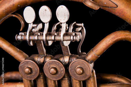 Vintage bronze pipes, valve, key mechanical elements french horn, black background. Good pattern, prompt music instrument. photo