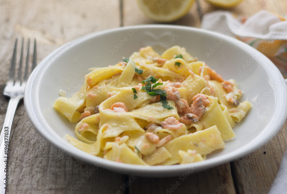 Homemade italian pasta with smoked salmone and creamy sauce and parsley on the top, white plate on the wooden rustic table Homemade italian pasta with smoked salmone and creamy sauce and parsley on the top, white plate on the wooden rustic table