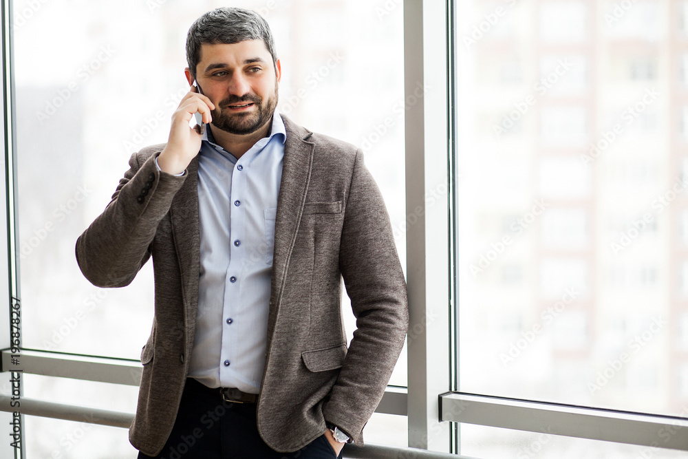 Man holding phone - young businessman using smartphone in office. Casual urban professional business man texting cellphone happy inside office banner panorama with copy space on background Man holding phone - young businessman using smartphone in office. Casual urban professional business man texting cellphone happy inside office banner panorama with copy space on background