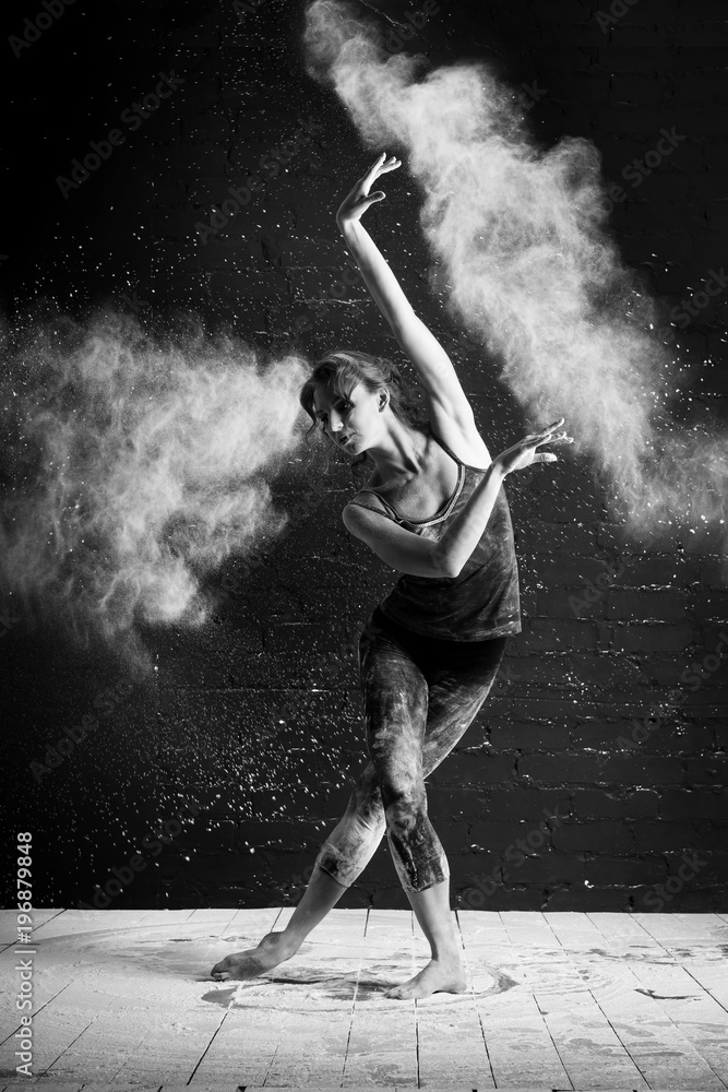beautiful ballet dancer dancing barefoot on black background in a cloud of dust