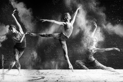beautiful ballet dancer dancing barefoot on black background in a cloud of dust