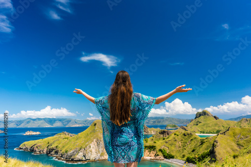 Rear view of a happy tourist enjoying the breeze while standing with outstretched arms outdoors during summer vacation in Padar Island, Indonesia