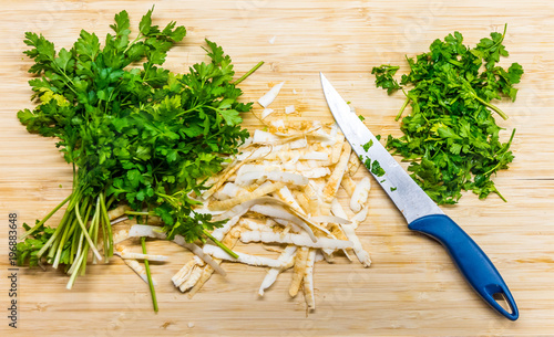 Parsley placed on the wooden desk with the knife near. Sharpened parsley prepared for cooking. Fresh and healthy plant