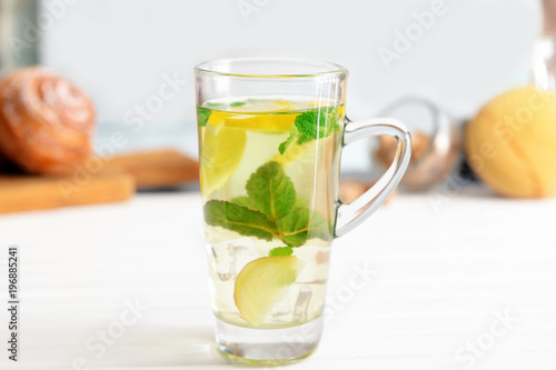 Glass cup of cold mint tea with lemon and ginger on table