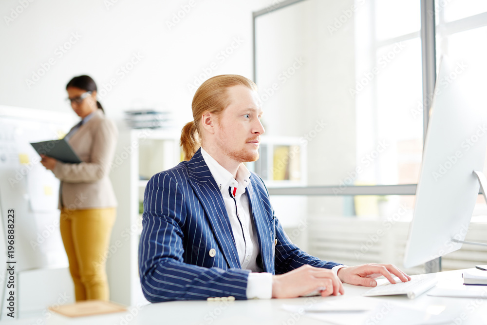 Businessman using computer at the table with woman in the background Businessman using computer at the table with woman in the background
