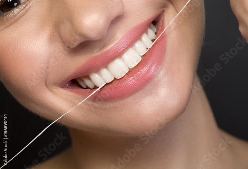 Close up of white healthy teeth of joyful young woman. She is using dental floss. Oral hygiene concept