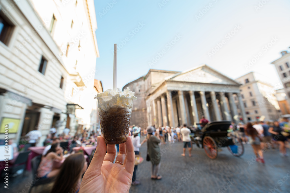 Fototapeta premium Appetizing coffee ice cream in female hand over Pantheon city view, Rome, Italy. Tasty ice cream like a symbol of summer and italian dessert over roman street.