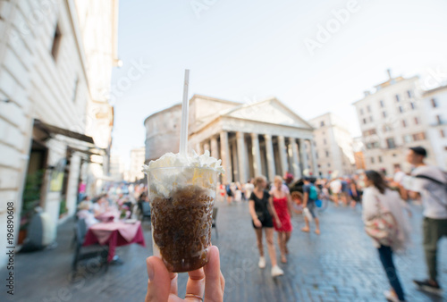 Appetizing coffee ice cream in female hand over Pantheon city view, Rome, Italy. Tasty ice cream like a symbol of summer and italian dessert over roman street.