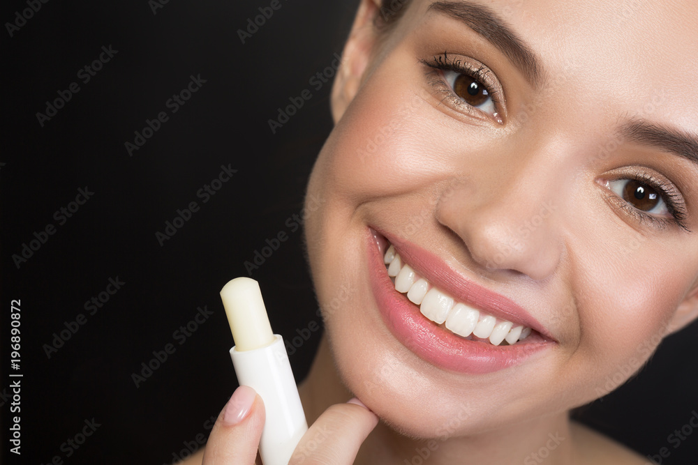 Close up portrait of cheerful attractive young woman is looking at camera with joy while holding hygienic lipstick. Beauty concept. Isolated background Close up portrait of cheerful attractive young woman is looking at camera with joy while holding hygienic lipstick. Beauty concept. Isolated background