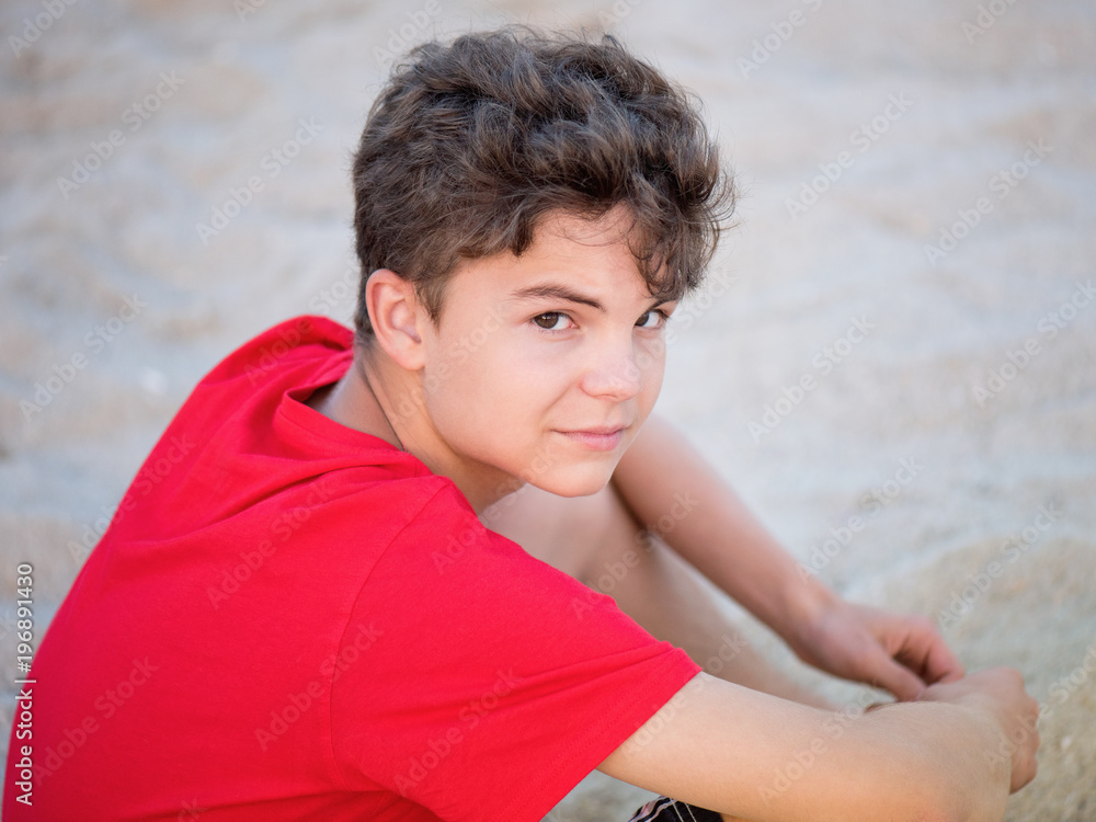 Teen boy on sand on beach - summer vacation, close-up portrait. Child looking up at camera. Teen boy on sand on beach - summer vacation, close-up portrait. Child looking up at camera.