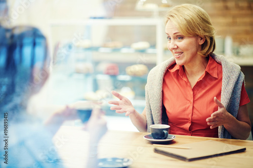 Woman communicating and drinking coffee with her friend at cafe