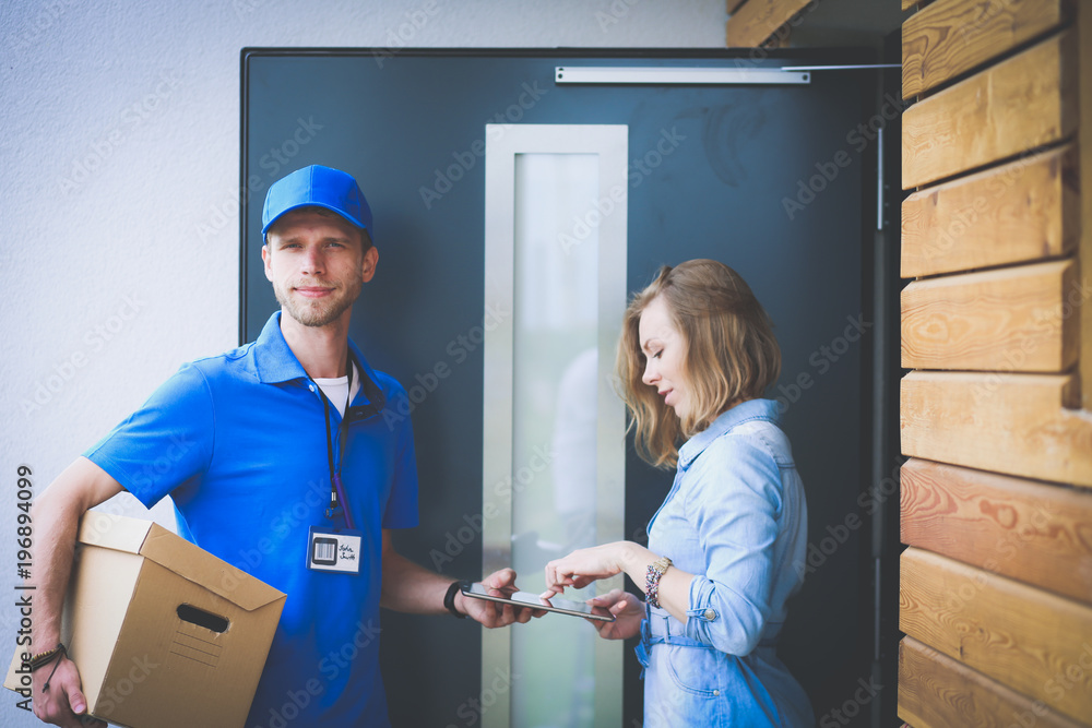 Smiling delivery man in blue uniform delivering parcel box to recipient - courier service concept Smiling delivery man in blue uniform delivering parcel box to recipient - courier service concept
