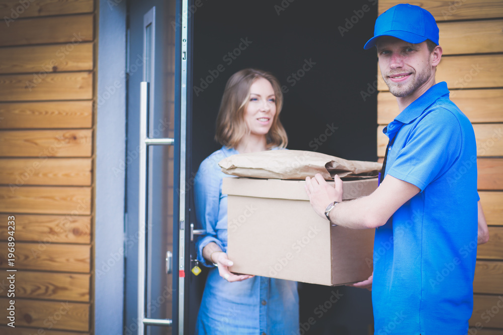 Smiling delivery man in blue uniform delivering parcel box to recipient - courier service concept Smiling delivery man in blue uniform delivering parcel box to recipient - courier service concept