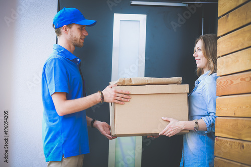 Smiling delivery man in blue uniform delivering parcel box to recipient - courier service concept © lenets_tan
