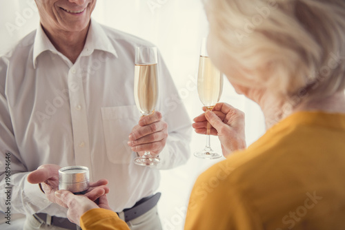 Happy elderly people standing with champagne while celebrating engagement. Male person giving jewelry box to woman
