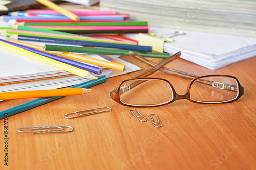 Glasses on the background of colored pencils and paper. The clutter on the desktop. 