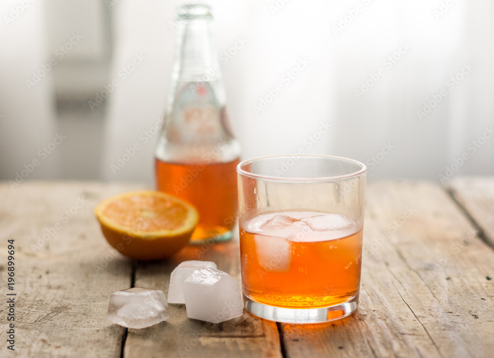 Glass of orange juice / cocktail san pelegrino with ice cubes and a bottle of in the background Glass of orange juice / cocktail san pelegrino with ice cubes and a bottle of in the background
