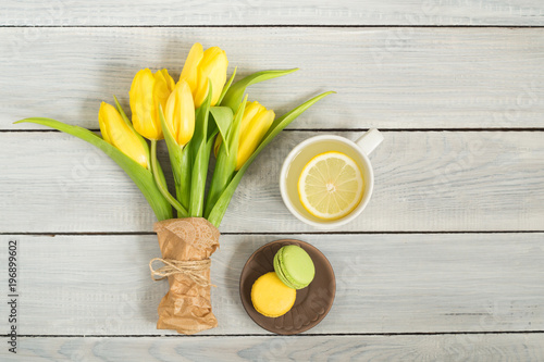 Yellow tulips, lemon tea and macarons on white wooden table