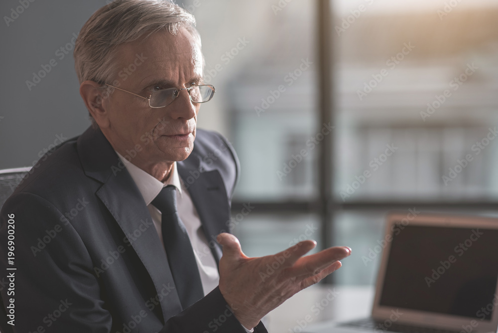 Portrait of focused old businessman gesticulating arms while locating indoor. Profession concept Portrait of focused old businessman gesticulating arms while locating indoor. Profession concept