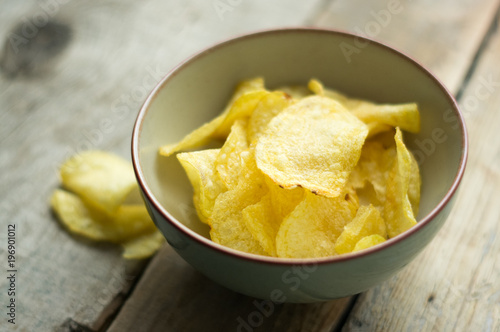 Isolated salted potato chips in a little bowl on the wooden background