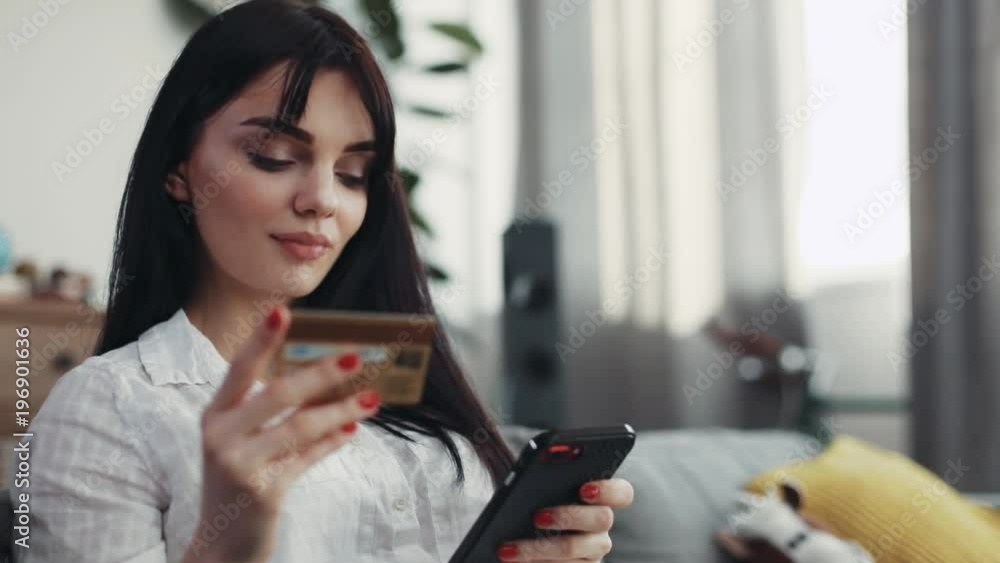 Brunette woman sitting on couch use phone and credit card at home beautiful telephone happy smartphone connection background business fashion hand happiness girl shopping money online pay attractive Brunette woman sitting on couch use phone and credit card at home beautiful telephone happy smartphone connection background business fashion hand happiness girl shopping money online pay attractive