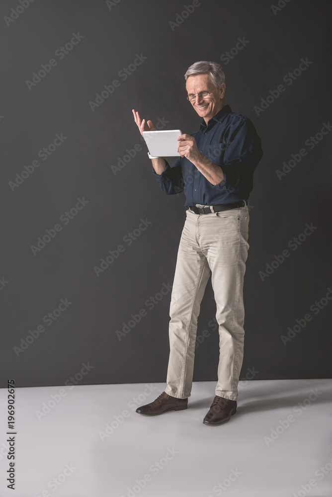 Full length portrait of beaming senior male using digital device while holding it in hands. Gadget and work concept Full length portrait of beaming senior male using digital device while holding it in hands. Gadget and work concept