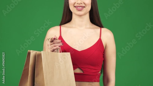 Cropped sclose up studio of a sexy woman in cropped top smiling showing thumbs up holding hopping bags posing on green chromakey screen consumerism purchasing buying shopaholic. photo