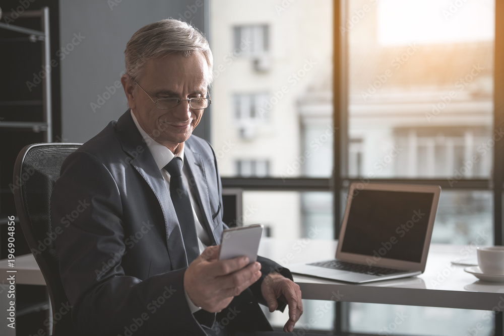 Portrait of smiling senior businessman using mobile while locating in office. Happy old employer and technology concept Portrait of smiling senior businessman using mobile while locating in office. Happy old employer and technology concept