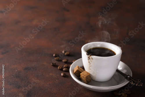 cup of black coffee on a saucer with brown sugar on a stone brown background