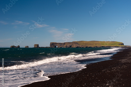 Volcanic rock on black sand beach at Vik in southern Iceland with eroded stone arch visible in distance