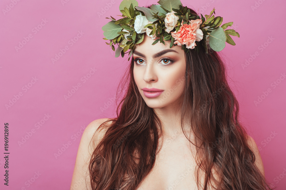 Portrait of beautiful young sexual sensual woman with perfect skin make up streaming hair and flowers on head on pink background. Wreath of flowers Spring Summer Fashion Lifestyle People concepts.