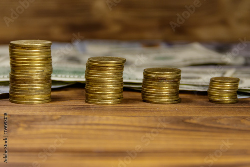 Stacks of golden coins and dollar bills on wooden background