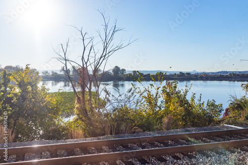 Train tracks and water river lake in Virginia with morning sun, reflection, plants in autumn photo