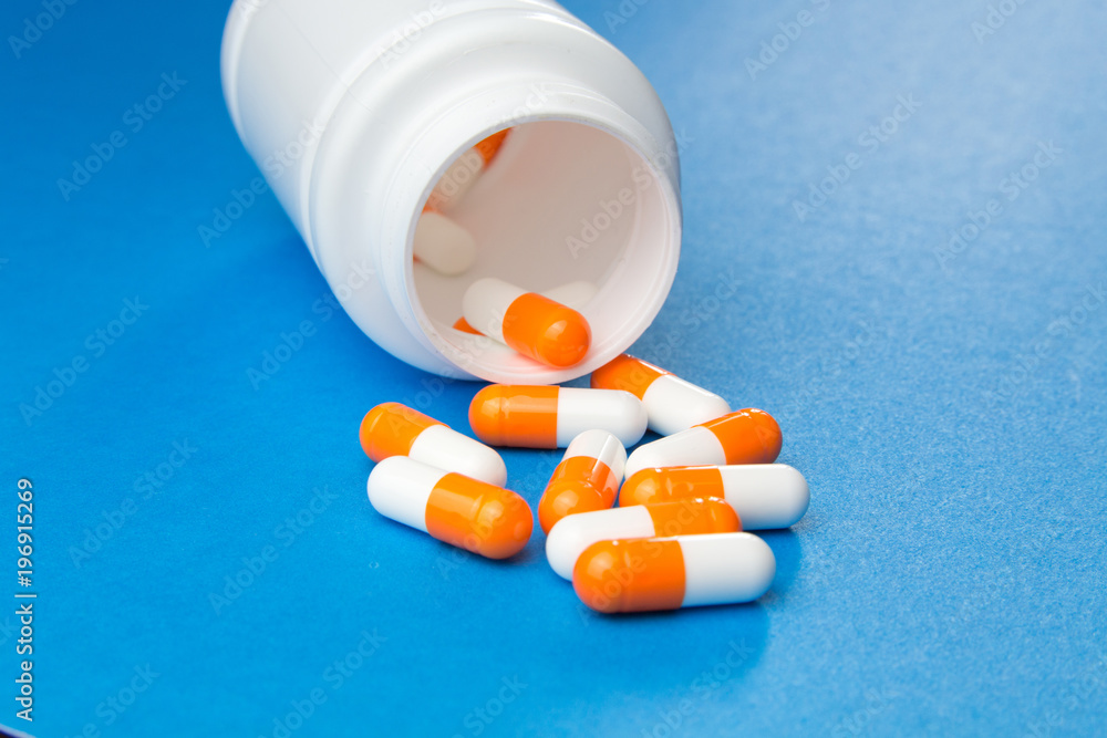 Orange white capsules (pills) were pored from a white bottle on a blue background. Medical background, template.Selective focus. Orange white capsules (pills) were pored from a white bottle on a blue background. Medical background, template.Selective focus.