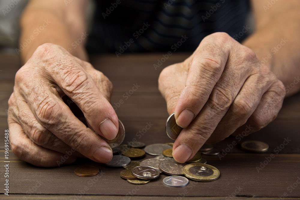 Hands of beggar with few coins. The concept of poverty . An elderly person on pension holds coins on wooden table background Hands of beggar with few coins. The concept of poverty . An elderly person on pension holds coins on wooden table background