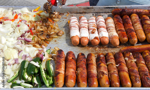 Street vendor cooking bacon wrapped hot dogs with onions and jalapeno peppers. Popular cuisine for street fairs and events