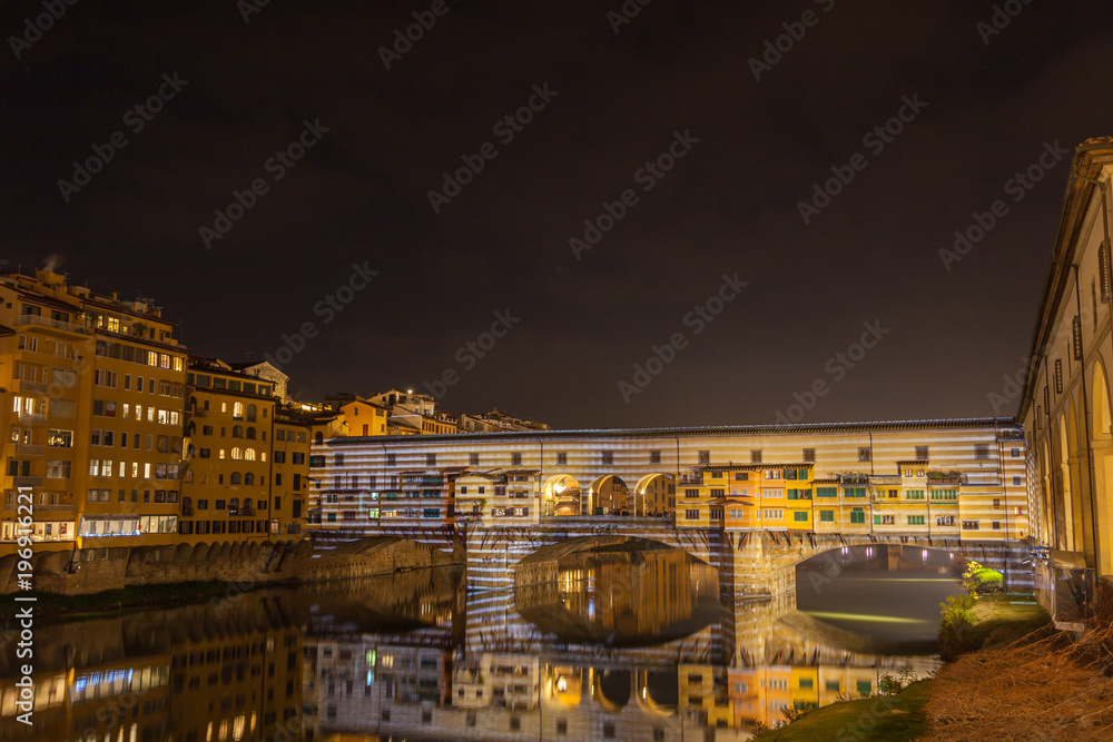 View at night of the landmark Ponte Vecchio with lights on it. Famous medieval bridge over the Arno river with old shops of artisan goldsmiths and jewelers, Florence, Italy.