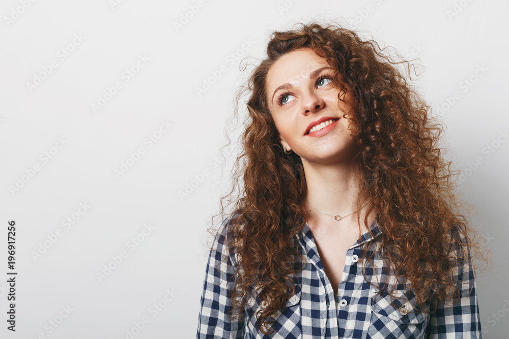 Dreamy curly woman with attractive look, dressed in checkered shirt, poses against white background, thinks about something pleasant. Good looking young female model being deep in thoughts Dreamy curly woman with attractive look, dressed in checkered shirt, poses against white background, thinks about something pleasant. Good looking young female model being deep in thoughts