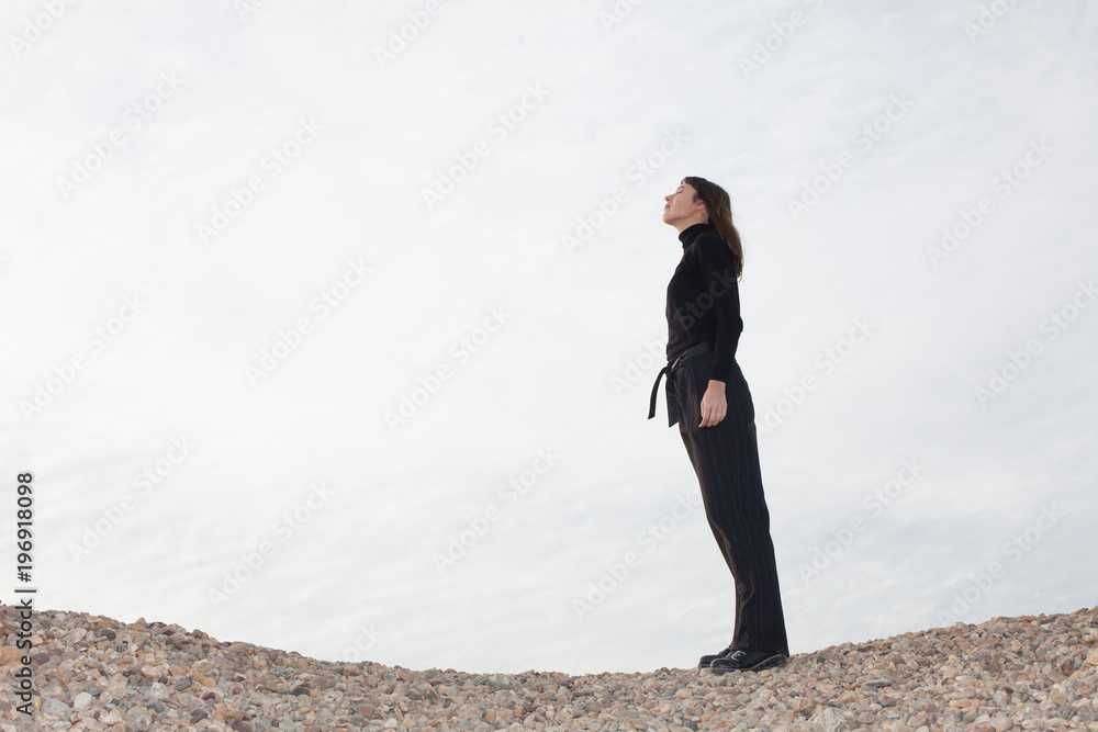 lone young woman standing on pebbles and enjoying the sun